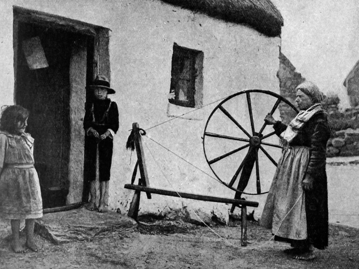 Rural Kerry life, 1880s — woman at spinning wheel outside thatched cottage